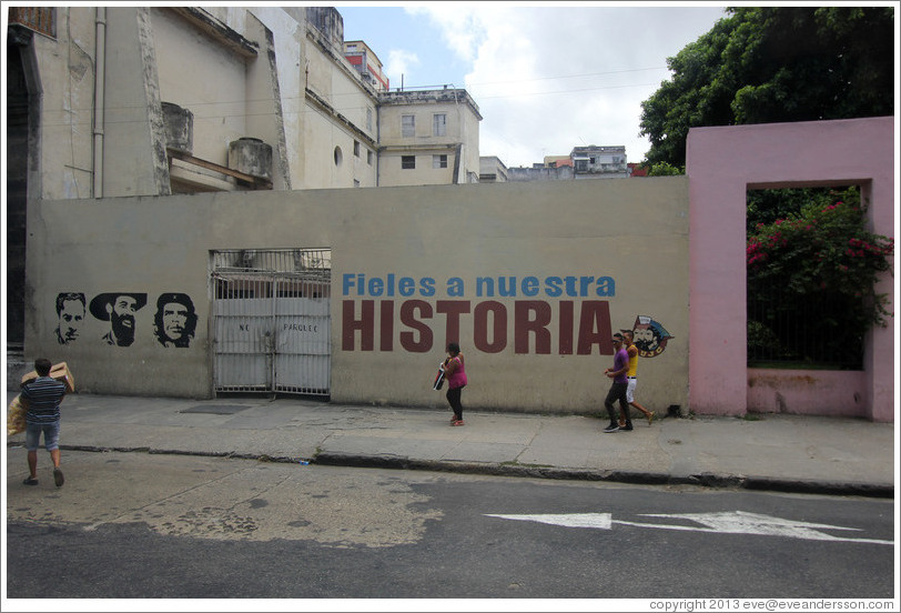 People walking past words painted on a wall saying "Fieles a nuestra historia" ("Faithful to our history"), Avenida Simon Bolivar (Calle Reina).