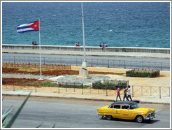 Cuban flag and a yellow and black taxi on the Malec&oacute;n.