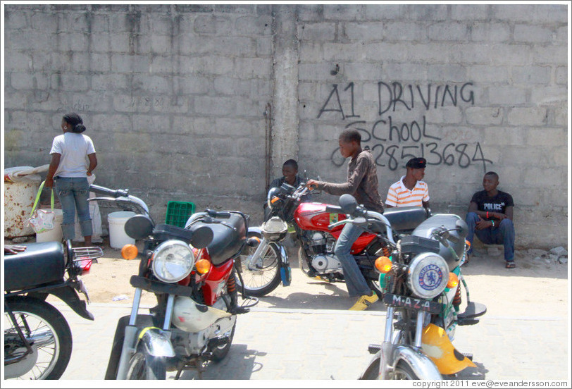 Kids and motorcycles in front of A1 Driving School written on a wall. Victoria Island.