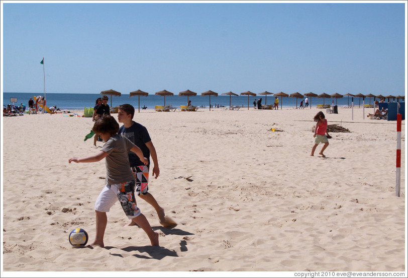 Kids playing soccer on the beach.
