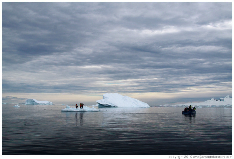 Three people standing on an icerberg, next to the zodiac from which they arrived.