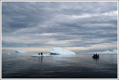 Three people standing on an icerberg, next to the zodiac from which they arrived.