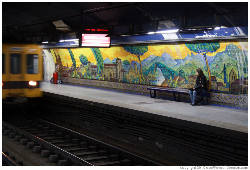 Young woman sitting in front of a mural called Paisajes de Espa?Mariano Moreno station, Subte (Buenos Aires subway).