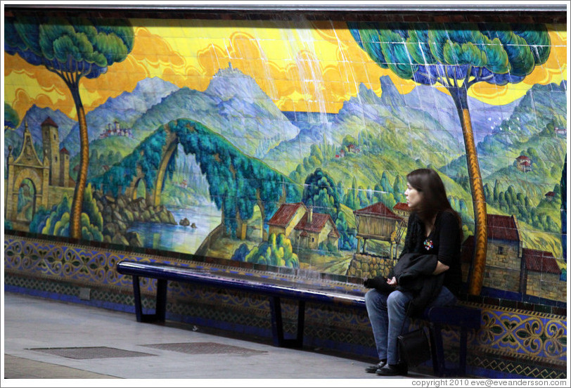 Young woman sitting in front of a mural called Paisajes de Espa?Mariano Moreno station, Subte (Buenos Aires subway).