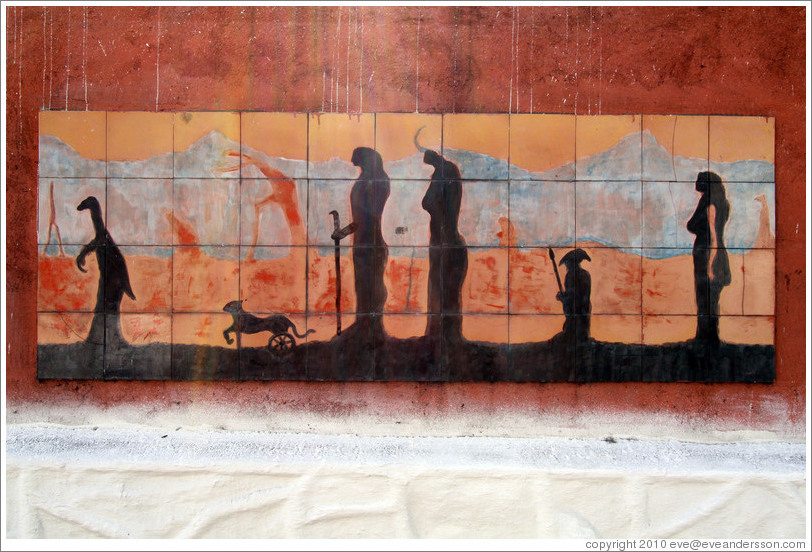 Artwork: silhouettes of a dinosaur, a feline with wheels for back legs, and people.  Wall surrounding the Cemit?o S?Paulo.