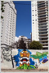Graffiti: creature with pointed teeth and green tubes.  Buildings in the background.  Av. H?o Pellegrino at Rua Marcos Lopes.