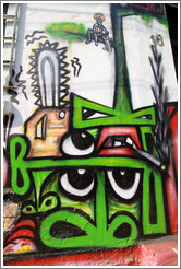 Graffiti: many green noses, a few eyes, a couple mouths, a cigarrette, a chainsaw, and a person sawing off the tree branch he's sitting on with a handsaw.  Villa Magdalenda neighborhood.  Rua Belmiro Braga and Rua Cardeal Arcoverde.
