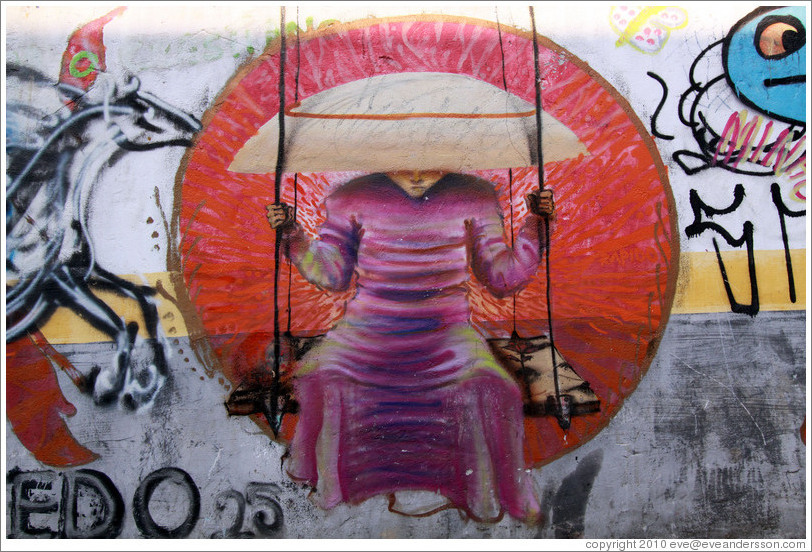Graffiti: monk on a swing wearing a takuhatsu hat.  Villa Magdalenda neighborhood.  Rua Padre Jo?Gon?ves near Rua Fradique Coutinho.