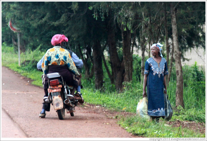 Man and woman on a motorcycle talking with a woman at the side of the road.