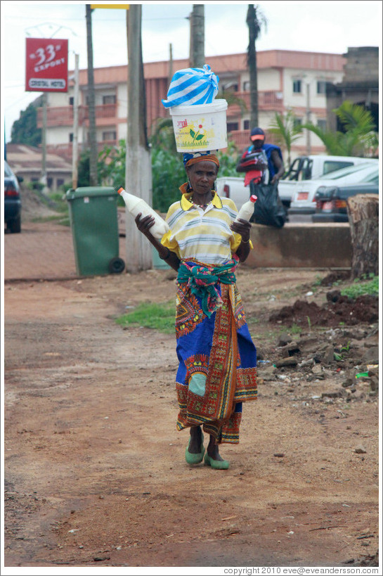 Woman with a bucket on her head and bottles in her hands.