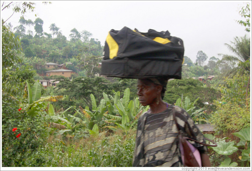 Woman carrying a duffel bag on her head.