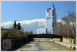 Looking east along the Mapocho River toward the mountains and a building with a Chilean flag.