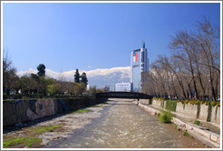 Looking east along the Mapocho River toward the mountains and a building with a Chilean flag.