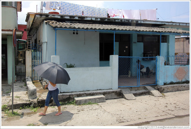 Woman with umbrella walking past blue house.