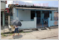Woman with umbrella walking past blue house.