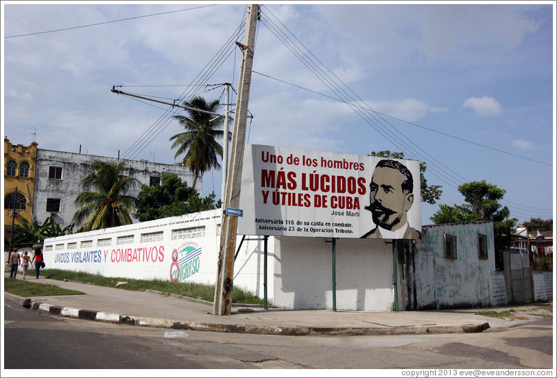 On Avenida de la Independencia, a wall painted with "Unidos, Vigilantes, y Combativos" ("United, Vigilant, and Combative"), "8 Congreso" ("8th Congress"), "En cada barrio" ("In every neighborhood"), and "CDR" (Committees for the Defense of the Revolution); and a billboard with Jos&eacute; Mart&iacute; next to the words "Uno de los hombres m&aacute;s l&uacute;cidos y &uacute;tiles de Cuba" ("One of the most lucid and useful men of Cuba"), "Aniversario 116 de su ca&iacute;da en combate" ("116th anniversary of his death in combat"), and "Aniversario 23 de la Operaci&oacute;n Tributo" ("23rd anniversary of the Operation Tribute").