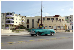 Green car passing beige buildings on the Malec&oacute;n.