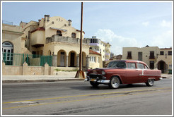 Red car passing beige buildings on the Malec&oacute;n.