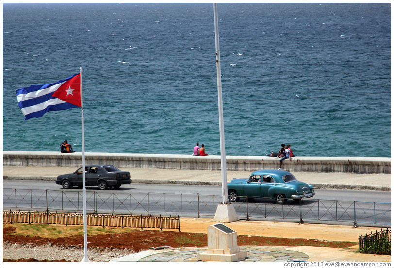 Cuban flag and black and blue cars on the Malec&oacute;n.