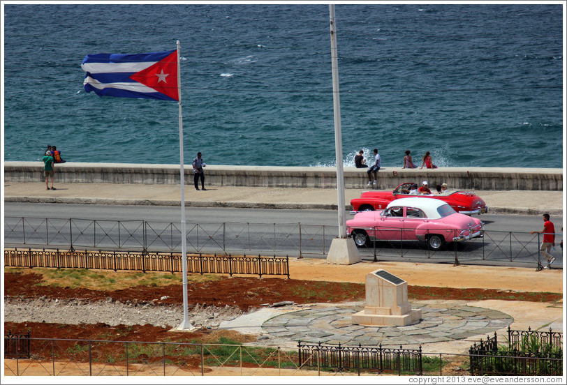 Cuban flag and pink and red cars on the Malec&oacute;n.