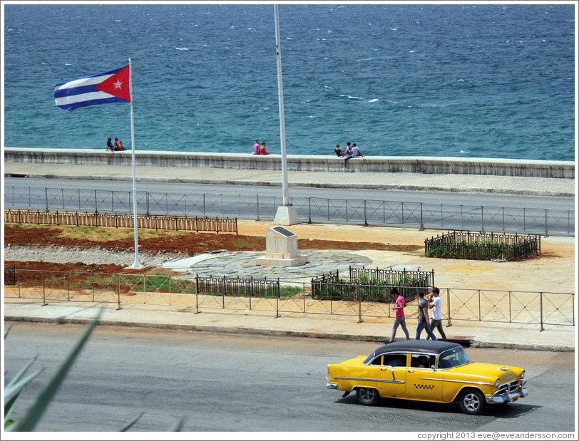 Cuban flag and a yellow and black taxi on the Malec&oacute;n.