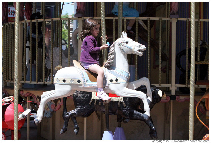 Girl riding a horse on the merry-go-round.  Place de la Rotonde.