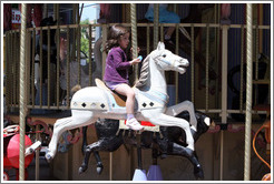 Girl riding a horse on the merry-go-round.  Place de la Rotonde.