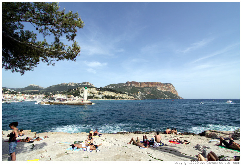 Sunbathers on the calanques, with a lighthouse in the background.