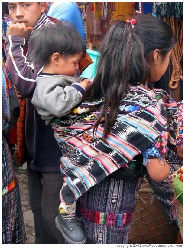 Young girl, wearing baby on back.