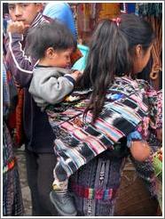 Young girl, wearing baby on back.