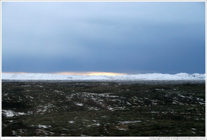 Volcanic terrain and snow-covered mountains, with a sliver of sunlight.