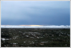 Volcanic terrain and snow-covered mountains, with a sliver of sunlight.