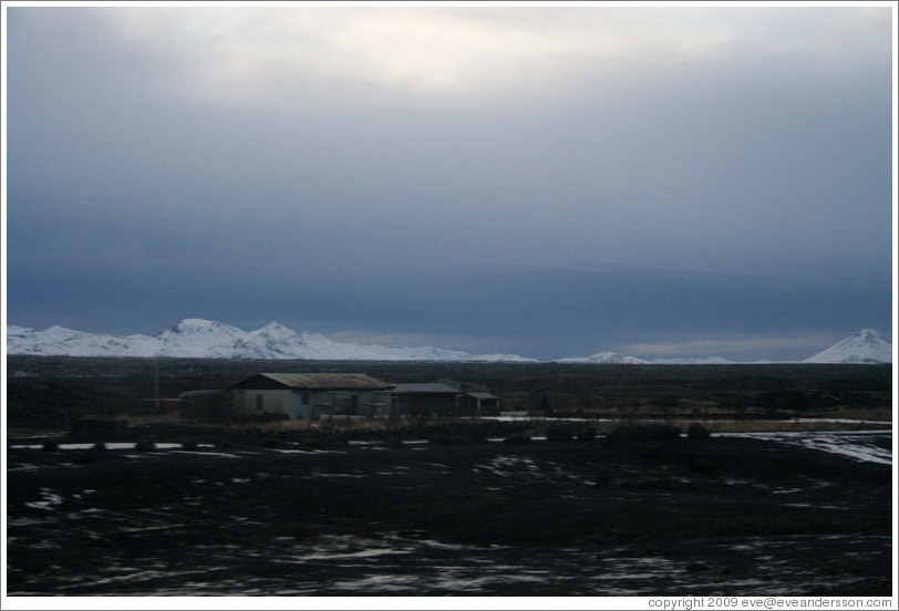 Volcanic terrain with metal hut and and snow-covered mountains.