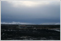 Volcanic terrain with metal hut and and snow-covered mountains.