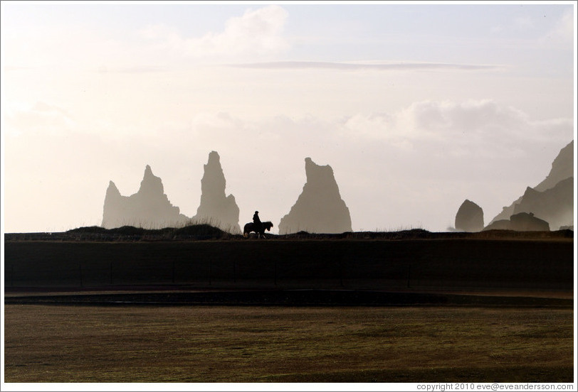 Reynisdrangar, volcanic rock shooting from the ocean, with a horseback rider passing in front.