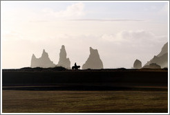 Reynisdrangar, volcanic rock shooting from the ocean, with a horseback rider passing in front.