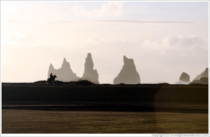 Reynisdrangar, volcanic rock shooting from the ocean, with a horseback rider passing in front.