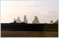 Reynisdrangar, volcanic rock shooting from the ocean, with a horseback rider passing in front.