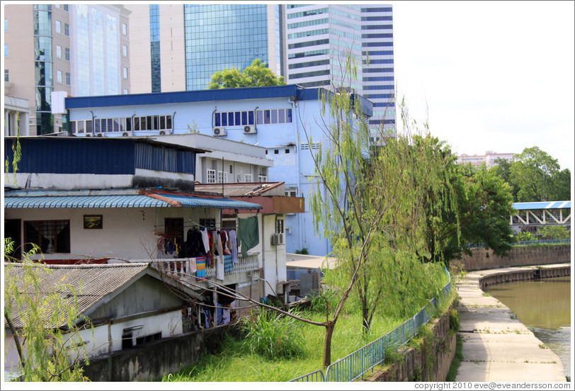 House with hanging clothes in front of a skyscraper on the bank of the Sungai Kelang, near Jalan Dang Wangi.
