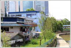 House with hanging clothes in front of a skyscraper on the bank of the Sungai Kelang, near Jalan Dang Wangi.