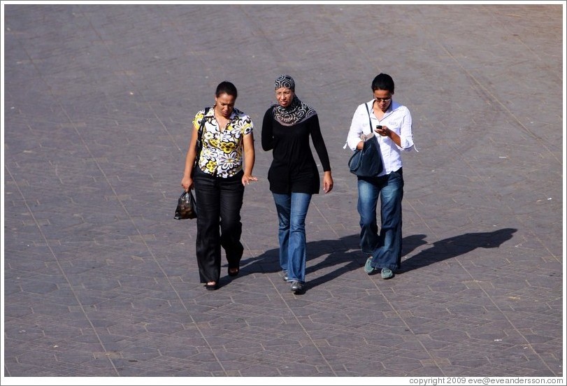 Three women walking, two without headdresses.  Jemaa el Fna.