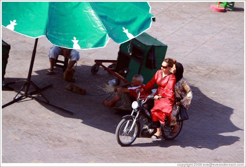 Women on a scooter, riding near man with monkeys, Jemaa el Fna.