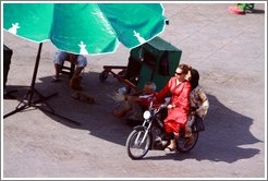 Women on a scooter, riding near man with monkeys, Jemaa el Fna.