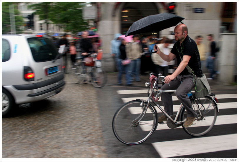 Bicyclist holding umbrella.  Dam Square, Centrum district.