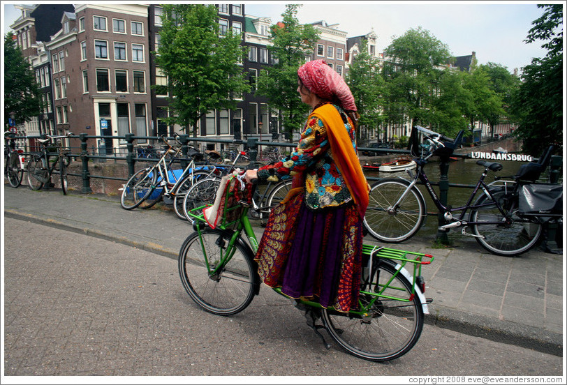 Colorfully dressed woman riding bicycle.  Bridge over Singel canal, Centrum district.