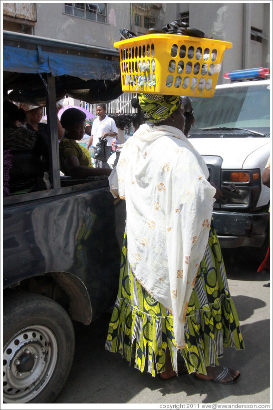 Woman balancing yellow basket on her head.
