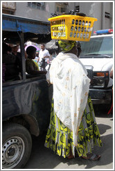 Woman balancing yellow basket on her head.