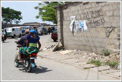 Couple on a motorcycle driving past A1 Driving School written on a wall. Victoria Island.