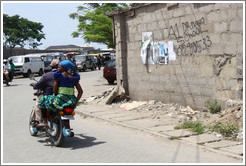 Couple on a motorcycle driving past A1 Driving School written on a wall. Victoria Island.