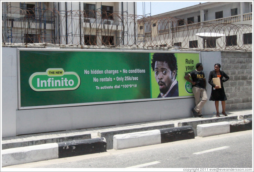 Man and woman speaking in front of a billboard, Maroko Road, Victoria Island.